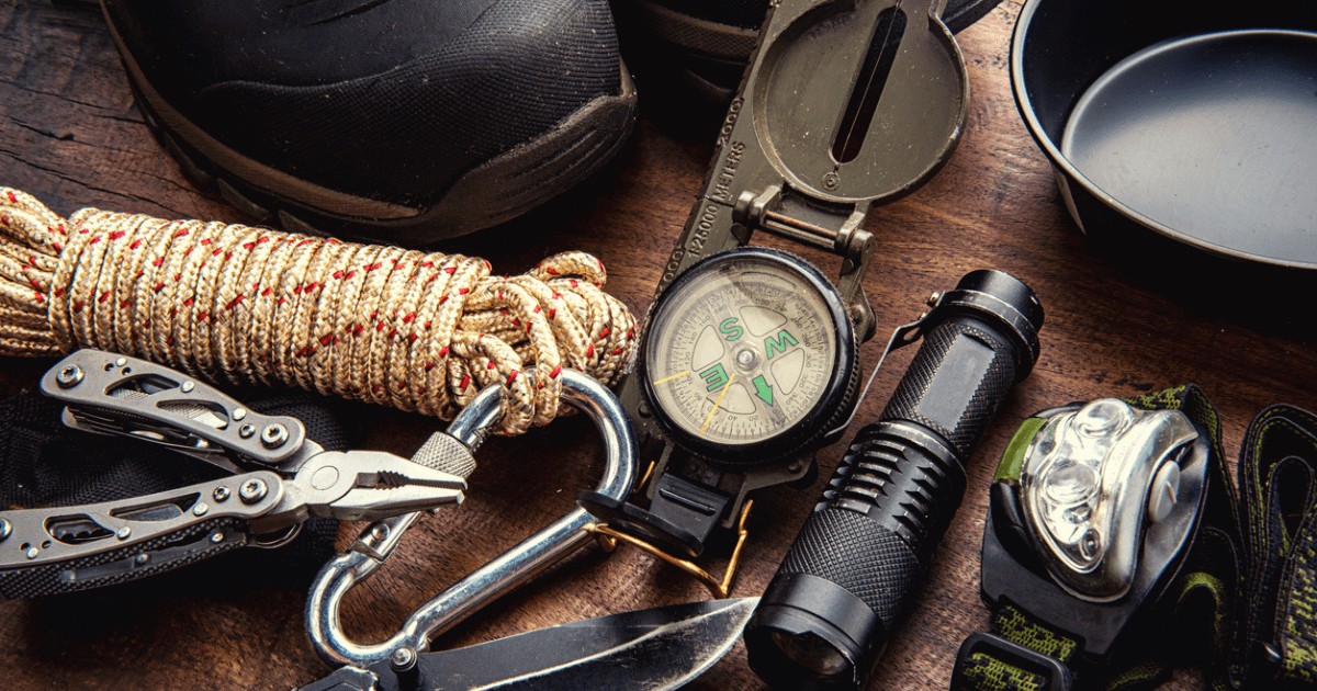 A table filled with bug out bag essential items like a compass, rope, shoes, and knife.