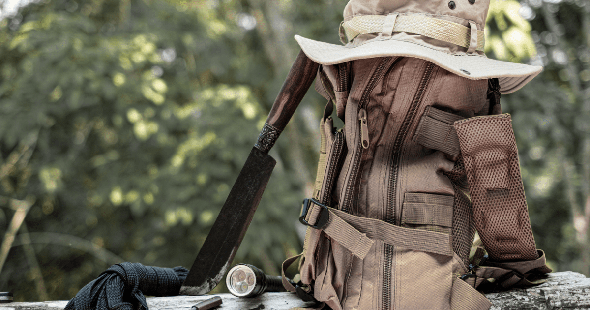 A bucket hat laying on a bug out bag next to a rifle.