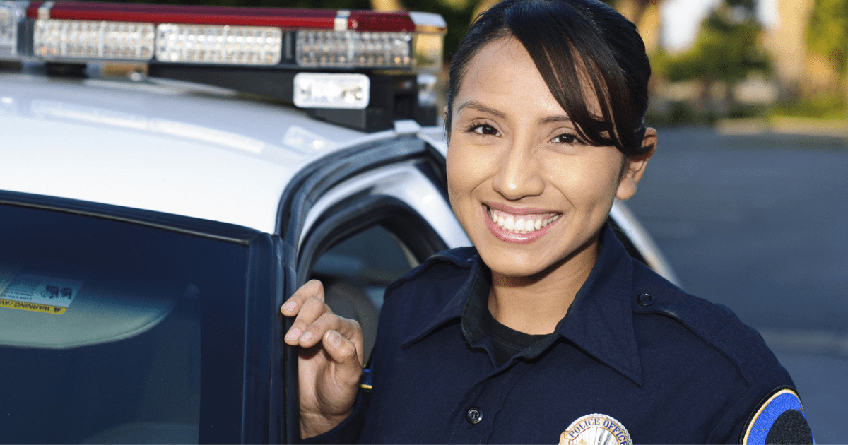 A smiling female police officer standing next to her patrol car.