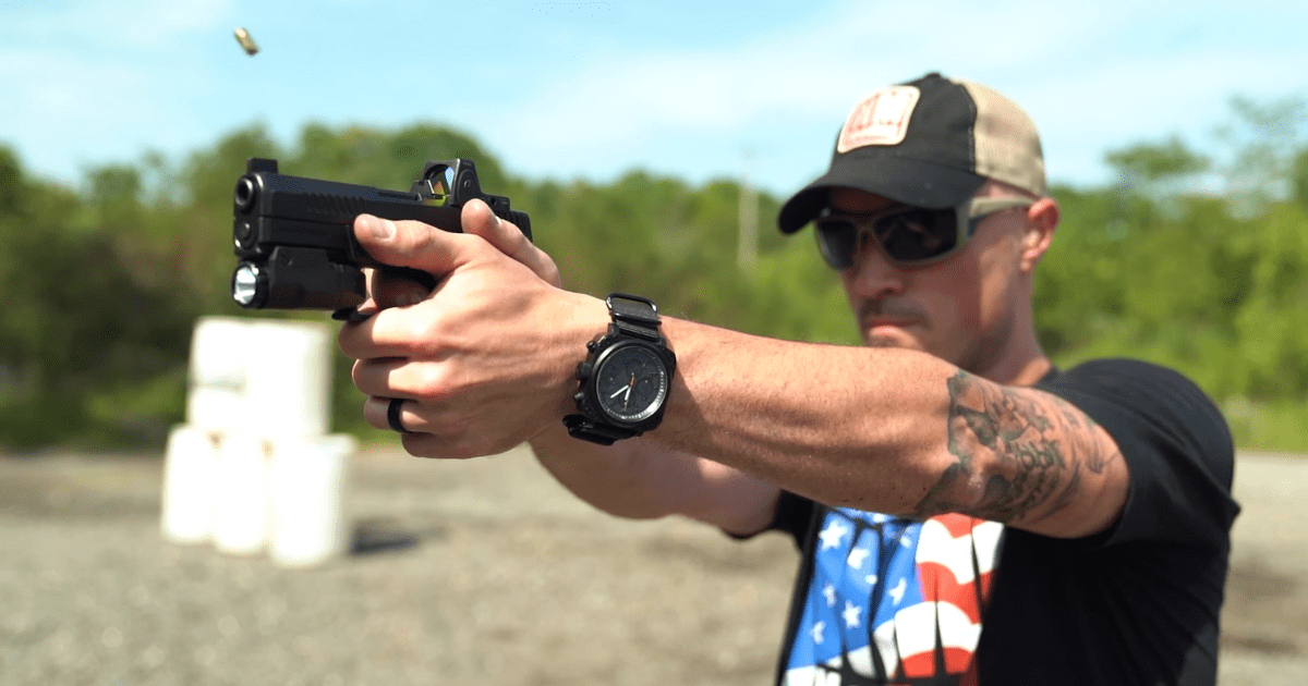 A man in a hat and black tshirt pointing his gun on a shooting range.