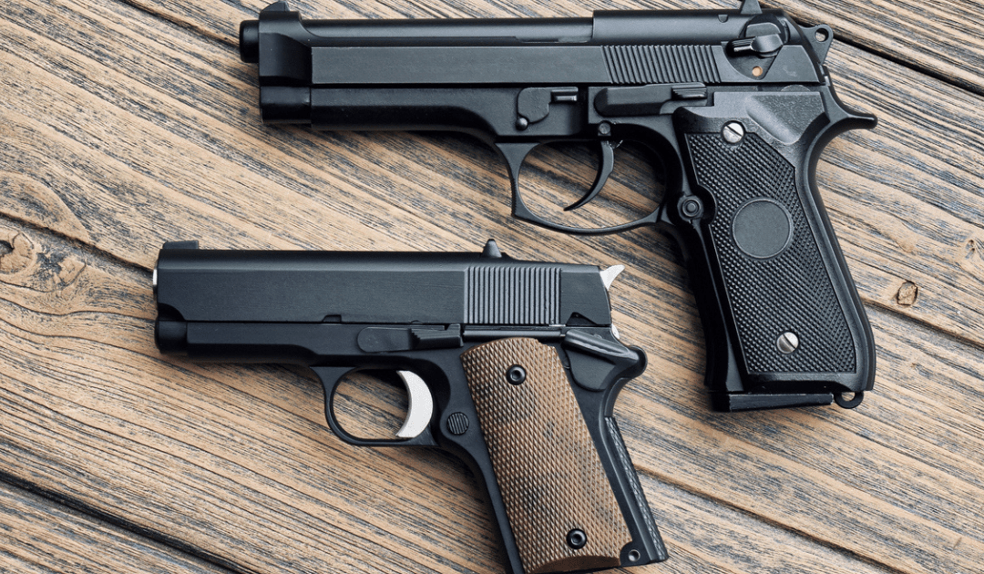 Two handguns of different sizes laying on a brown table.