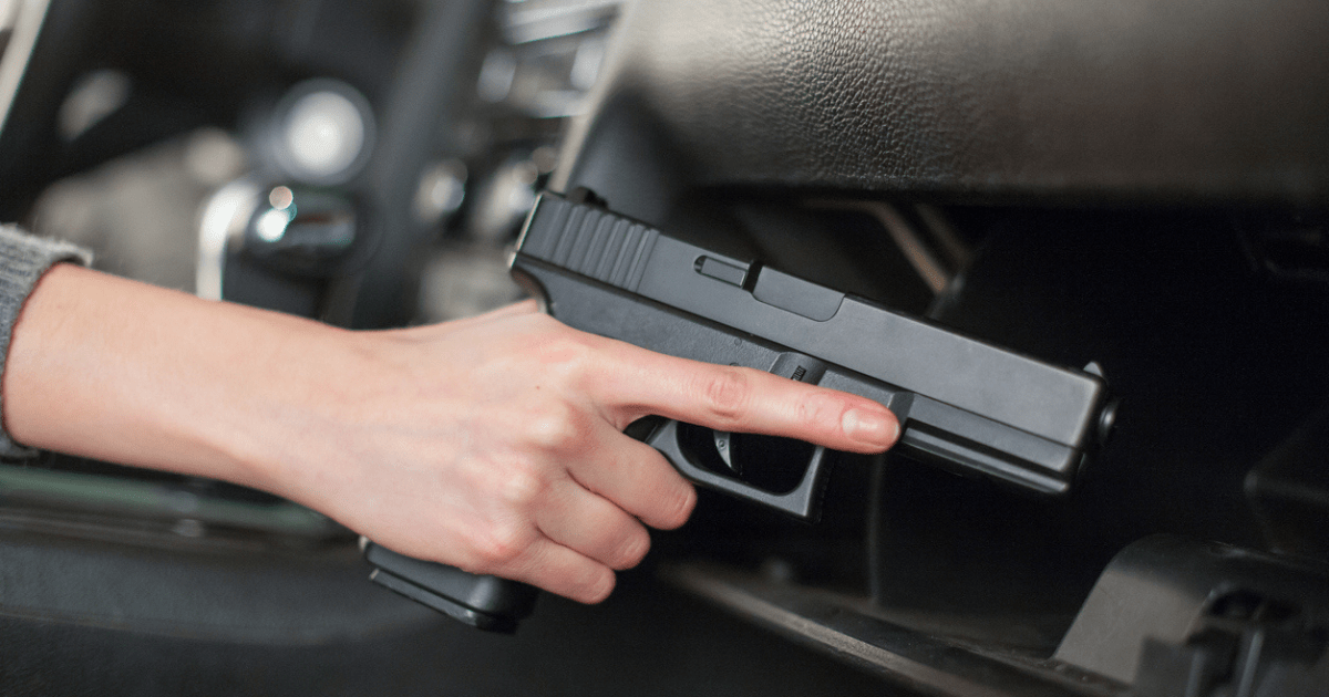 A woman placing her gun into her glovebox holster in her truck.