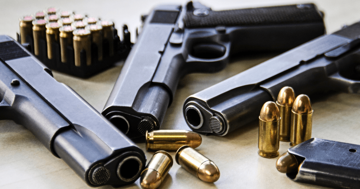 Three guns laying on a table surrounded by ammo.