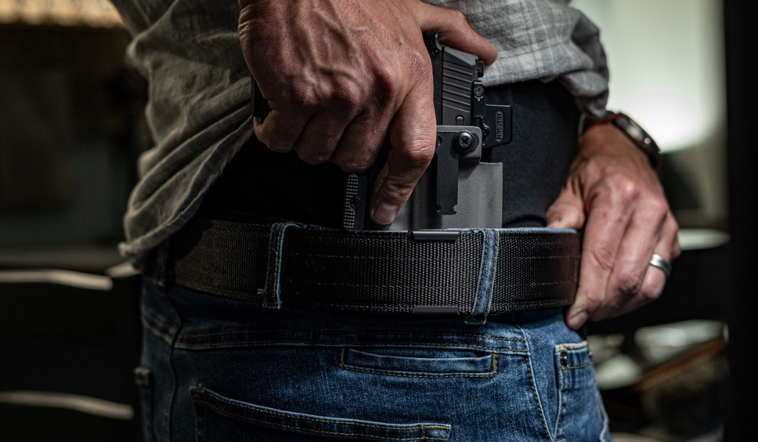 A man holstering his concealed carry firearm on his hip.