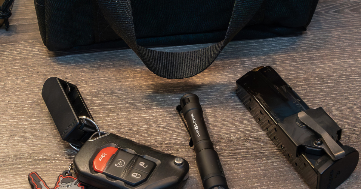 Car keys, tactical light, spare magazine with a NeoMag attached, and black range bag on a table.